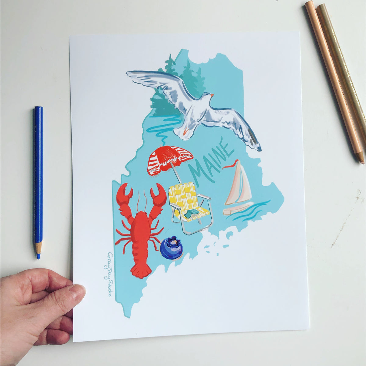 State of Maine artowrk featuring a seagull, sailboat, lobster, blueberry, beach chair and umbrella.