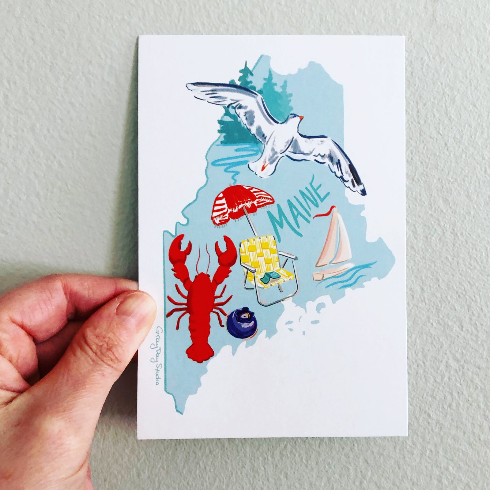 Maine state postcard complete with a seagull, lobster, blueberry, sailboat, beach chair and beach umbrella!. Made in Maine by local artist Abigail Gray Swartz.